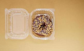 Chocolate donut in a plastic container on a brown or coffee background photo