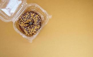 Chocolate donut in a plastic container on a brown or coffee background photo