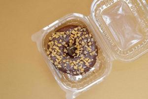 Chocolate donut in a plastic container on a brown or coffee background photo