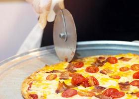Primer plano de la mano del chef cortando pizza en la cocina foto