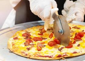 Primer plano de la mano del chef cortando pizza en la cocina foto