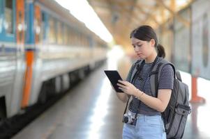 Una viajera extranjera lleva una mochila con una tableta mientras espera el tren. foto
