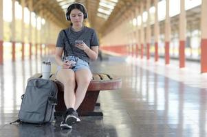 una joven viajera escucha música con auriculares mientras espera su viaje en la plataforma. foto