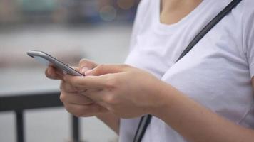 jonge aziatische vrouw die smartphone in openlucht openbaar park gebruikt. slow-motion close-up. zoeken op internet, online technologie. video