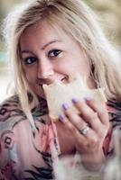 mujer rubia sosteniendo y comiendo un sándwich, mirando a la cámara. cerrar sesión de retrato. foto