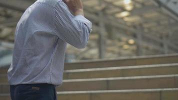 hombre de negocios asiático caminando y usando el teléfono inteligente. Retrato de cámara lenta empresario asiático contesta el teléfono. Hombre asiático con gafas usa el teléfono en la calle cerca del gran edificio de oficinas. video