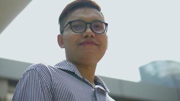 Slow-Motion-Porträt asiatischer Geschäftsmann lächelt und schaut in die Kamera, die auf einer städtischen Stadt steht. Aufnahmen mit niedrigem Winkel. video