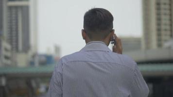 porträtt stilig asiatisk affärsman talar telefon med vän gå på urban stad. slowmotion -inspelning.
