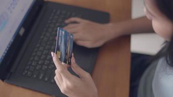 close-up handen jonge Aziatische meisje met behulp van laptop online winkelen met creditcard thuis. video