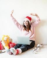 Mujer joven con gorro de Papá Noel de compras online rodeado de regalos foto