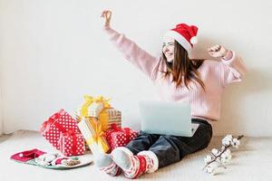 Mujer joven con gorro de Papá Noel de compras online rodeado de regalos foto