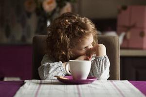 Little curly-haired girl sitting at the table photo