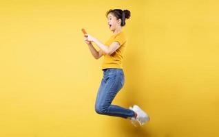 Full body profile photo of young asian girl jumping high holding a phone writing a new social media post, isolated on blue background