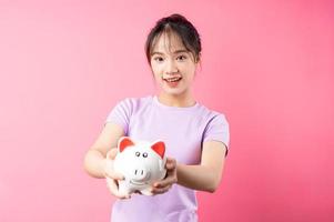 Portrait of girl holding piggy bank in hand, isolated on pink background photo