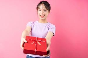 Portrait of cheerful girl holding gift box in hand, isolated on pink background photo