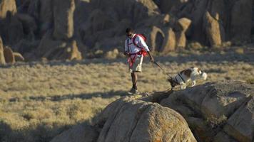 un joven mochilero en un desierto montañoso con su perro. video