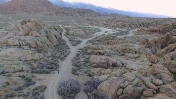 Toma aérea de un joven mochilero con su perro en un camino de tierra en un desierto montañoso. video