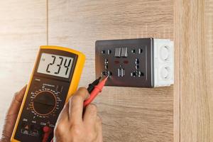 electricista usando un medidor digital para medir el voltaje en un enchufe de pared en una pared de madera. foto