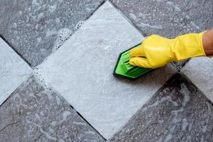 Cleaning the tiled floor with a green color plastic floor scrubber. photo