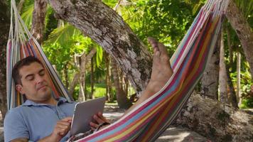 man zit in hangmat met behulp van digitale tablet, costa rica. geschoten op rood episch voor hoge kwaliteit 4k, uhd, ultra hd-resolutie. video