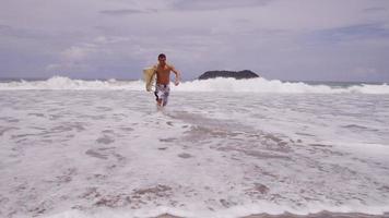 surfista che corre dall'oceano, rallentatore. girato in rosso epico per una risoluzione 4k, uhd, ultra hd di alta qualità. video