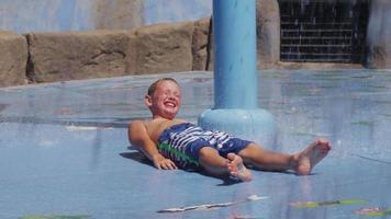 Boy laying down and getting splashed at fountain on summer day, slow motion video