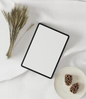 The tablets are placed on a white cloth with dried grass and pine cones. photo