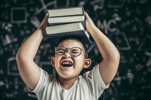 un niño con gafas estudió y se puso un libro en la cabeza en el aula. foto