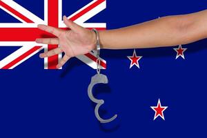 handcuffs with hand on New Zealand flag photo