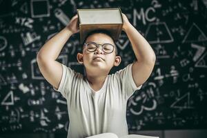 un niño con gafas estudió y se puso un libro en la cabeza en el aula. foto