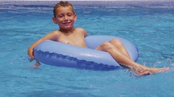 jeune garçon sur chambre à air dans la piscine. tourné sur red epic pour une résolution 4k, uhd, ultra hd de haute qualité. video