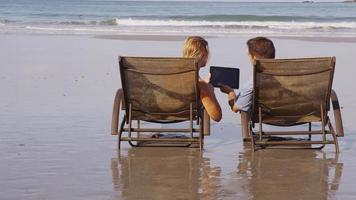 casal usando tablet digital na praia. filmado em vermelho épico para alta qualidade 4k, uhd, resolução ultra hd. video