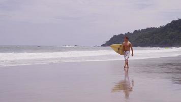 hombre con tabla de surf caminando en la playa. filmado en rojo épico para una resolución de alta calidad de 4k, uhd, ultra hd. video