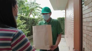 leveransman med ansiktsmask ger paket till en asiatisk kvinna.