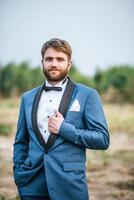 Guapo novio en traje de boda publicar en el parque foto