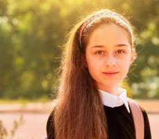 Schoolgirl in school clothes in nature on a background of leaves. Girl 11 years old. photo