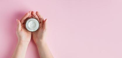 Female hands with a bottle of cream on pink background. Spa and body care concept. Image for advertising. photo