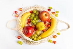 frutas maduras orgánicas en bolsa de malla ecológica sobre fondo blanco. bolso de hilo de moda para ir de compras. concepto de alimentación saludable y estilo de vida sostenible. cero desperdicio. foto