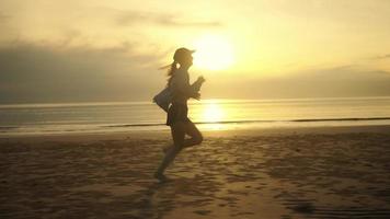 vista lateral a cámara lenta mujer descalza corriendo en la playa hay olas del mar, hay una luz crepuscular, el sol por la mañana o por la noche, estilo de vida en tiempo de vacaciones. video