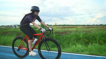 zijaanzicht volgen. Aziatische vrouwen oranje fietser met een beschermende helm oefentraining snel rijden op de wegen buiten de stad video