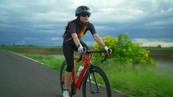 Seguimiento de vista de fuente.las mujeres asiáticas ciclista naranja con casco protector entrenamiento de ejercicio conducción rápida en las carreteras fuera de la ciudad video