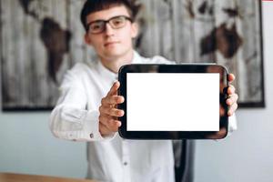 Young guy in glasses working in office showing tablet, copyspace photo