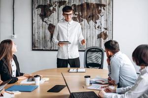 Young attractive guy in glasses with a tablet in his hands presents his project at a meeting photo