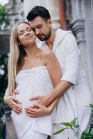 Husband hugs pregnant wife from back on balcony photo