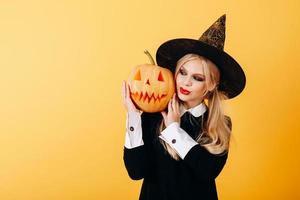 Woman portrait against a yellow background  holding pumpkin and looking on it smiling photo