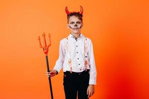 Devil boy standing against an orange background in masquerade makeup. Halloween concept photo