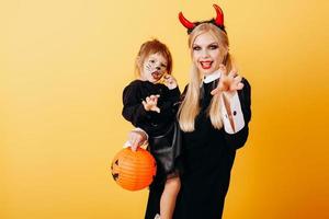 Happy emotion of devil woman standing against a yellow background and holding a little girl