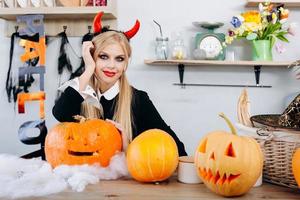 diablo mujer sentada en la mesa junto a calabazas mirando a la cámara.- concepto de halloween foto