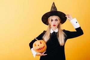 Wonder emotion of woman standing against a yellow background  holding pumpkin and touches her hat photo