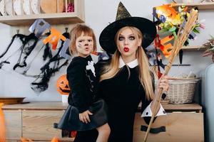 Mother and daughter make scary face standing  in fancy dress and looking at the camera. Woman holding a broom